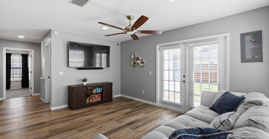 Living room with TV, couch, cabinets, and a ceiling fan in a modern home.