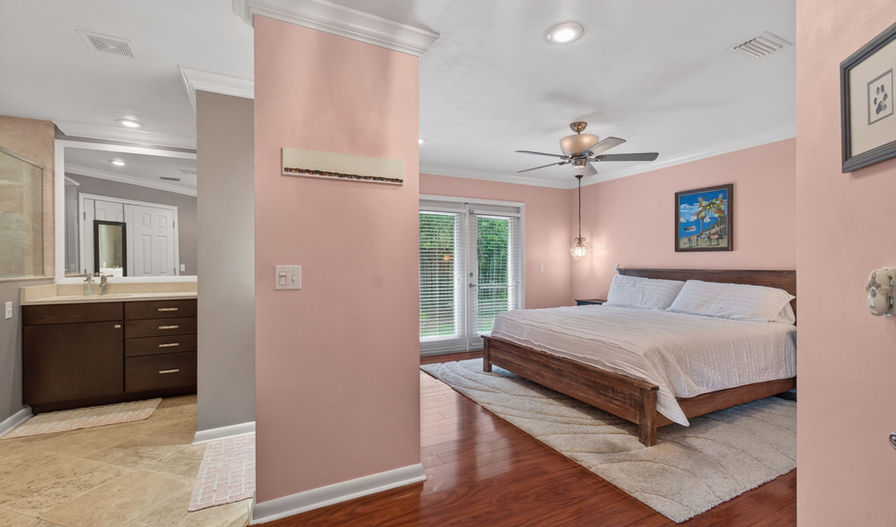 Bedroom with pink walls, wood floor, ceiling fan & ensuite bath