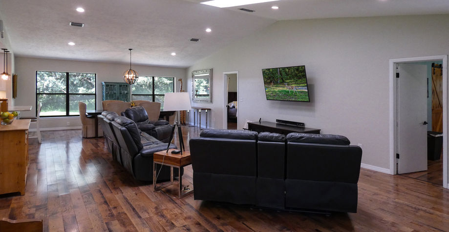 Spacious living room with hardwood floors, TV, and large windows.