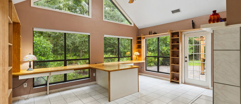 Spacious office area with large windows, desk, and vaulted ceiling. Natural light.