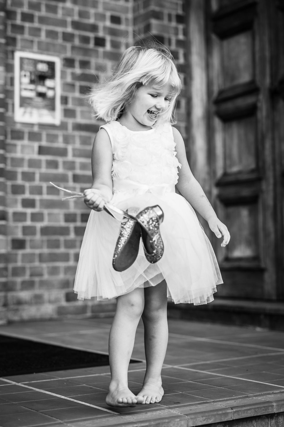 Little girl in a white dress laughing and holding her shoes