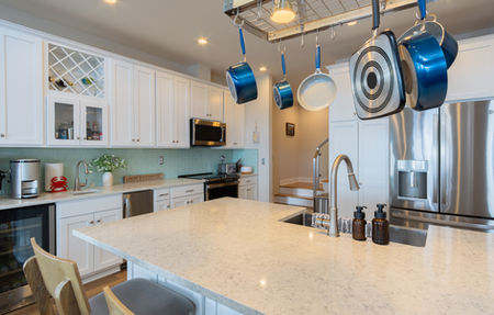 A wide view of a white kitchen island with a hanging pot rack above.