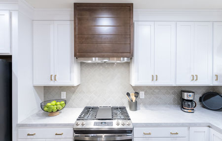 Close up of a dark wood range hood and white tile backsplash in a custom home.