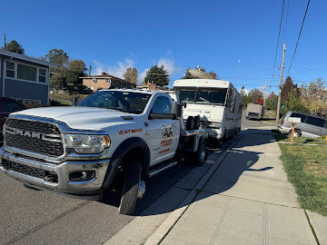 Tow truck pulling an RV on a sunny residential street, landscape, main focus on the truck and RV, blue sky, daytime