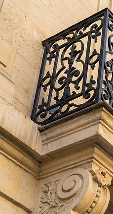 Balcon en fer forgé orné et façade d'immeuble, ciel bleu en arrière-plan.