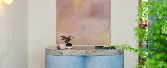 Blue podium. Pink wall mount and grey wall. Ferns on the side.