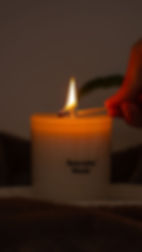 A specially made candle in a dark room, with a hand holding a lit match to its wick