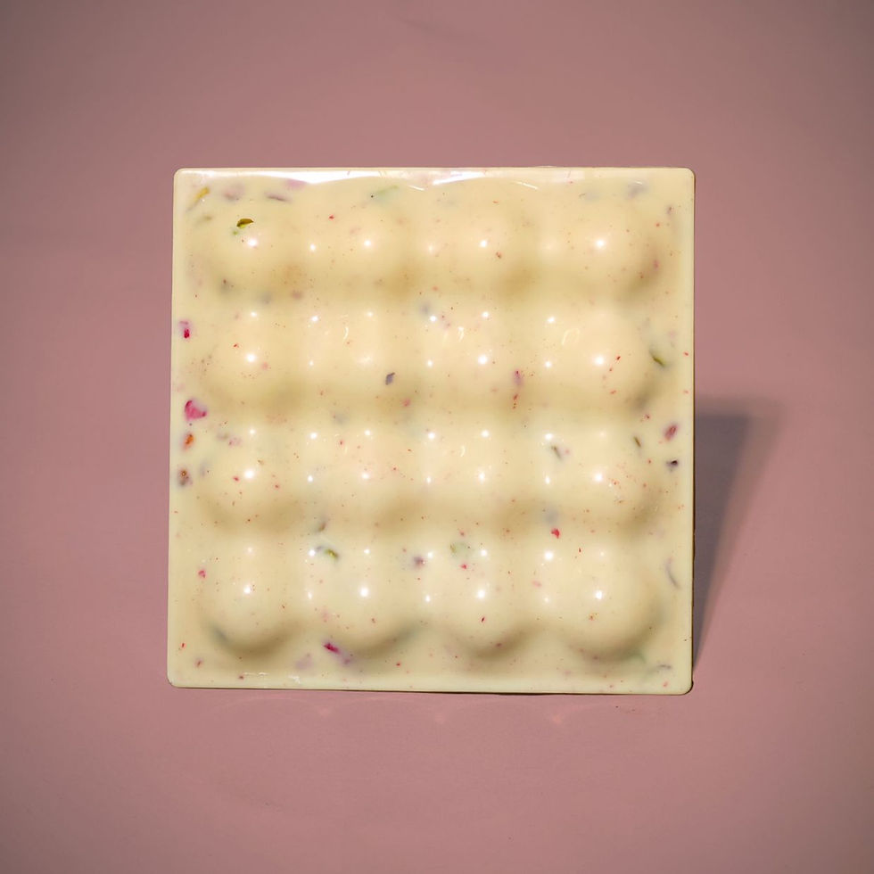 a square bubble bar of white chocolate with specs of raspberry and pistachio. Pink background