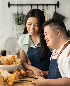 Woman in an apron helping a person with an intellectual disability bake croissants as part of a hospitality course