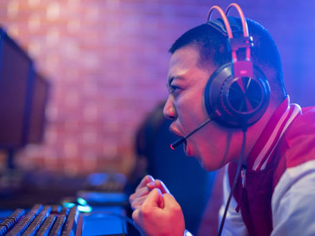 Young man cheering, commentating on an esports match. He's wearing a headset and is under red and blue lighting. One of the esports careers the article discusses.