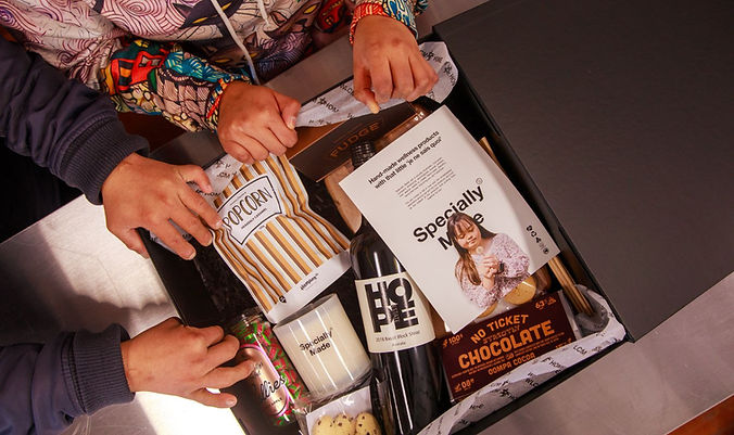 2 IDF of St George participants packing a hamper co hamper with popcorn, wine, chocolate, fudge, and biscuits