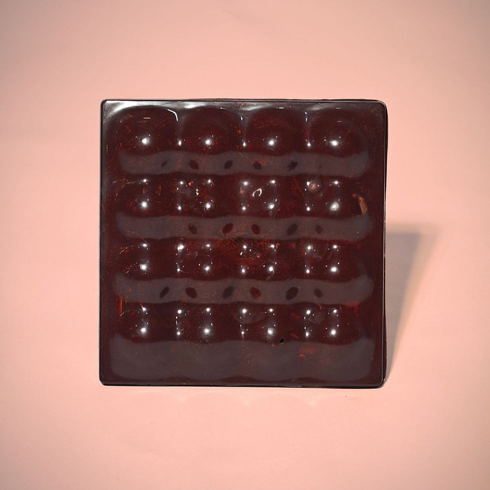 A square dark chocolate bar shining in the light. It is on a pink background