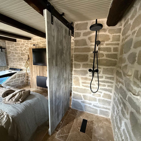 Grande douche à l'italienne en pierre avec barre et pommeau de douche à l'ancienne. La salle d'eau dispose également d'un meuble vasque en marbre.