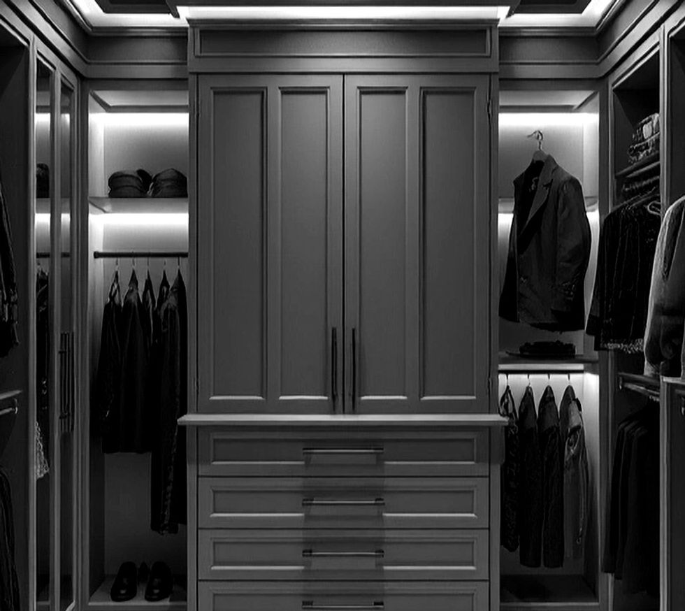 A wide view of a luxurious custom closet with grayscale theme, dim lighting, and white mar