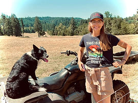 Tierney standing next to border collie while it sits on an ATV