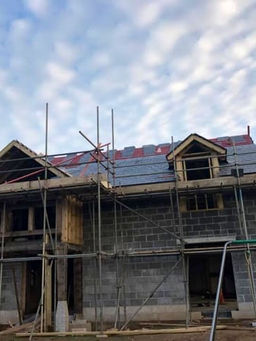 Under-construction house frame with scaffolding and roof timbering under a blue sky