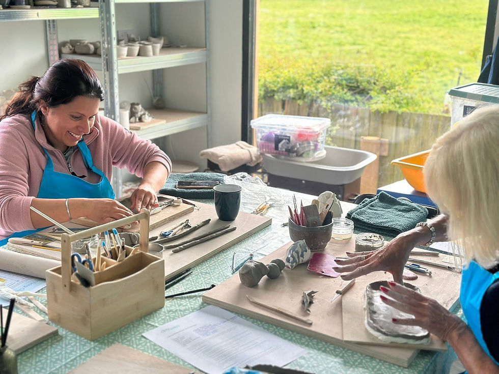 Two women in blue aprons shaping clay by hand at a workbench during a pottery workshop