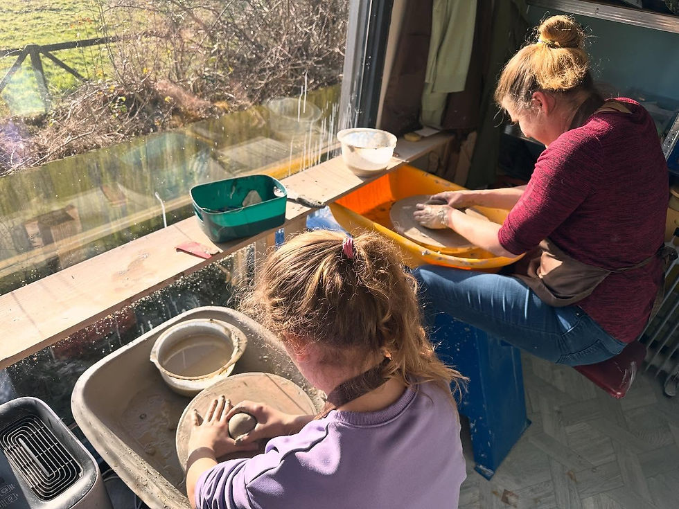High-angle view of two women shaping clay on pottery wheels by a bright window overlooking green fields