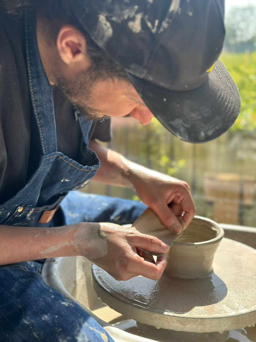 Close-up of a craftsman using a rib tool to smooth the side of a clay bowl on a pottery wheel