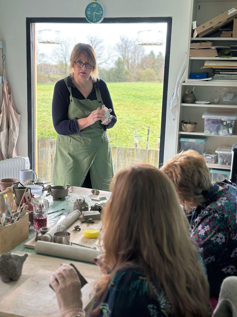 Pottery instructor in a green apron demonstrating a clay technique to students during a studio workshop