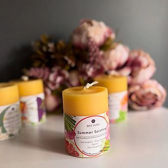 Summer Solstice pure beeswax candle with vibrant botanical essential oil label in front of blurry floral background