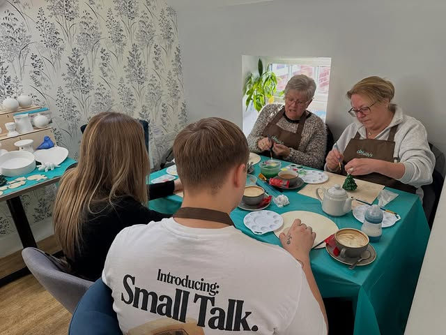 Group of people sitting around a table covered with a teal tablecloth enjoying a pottery painting workshop