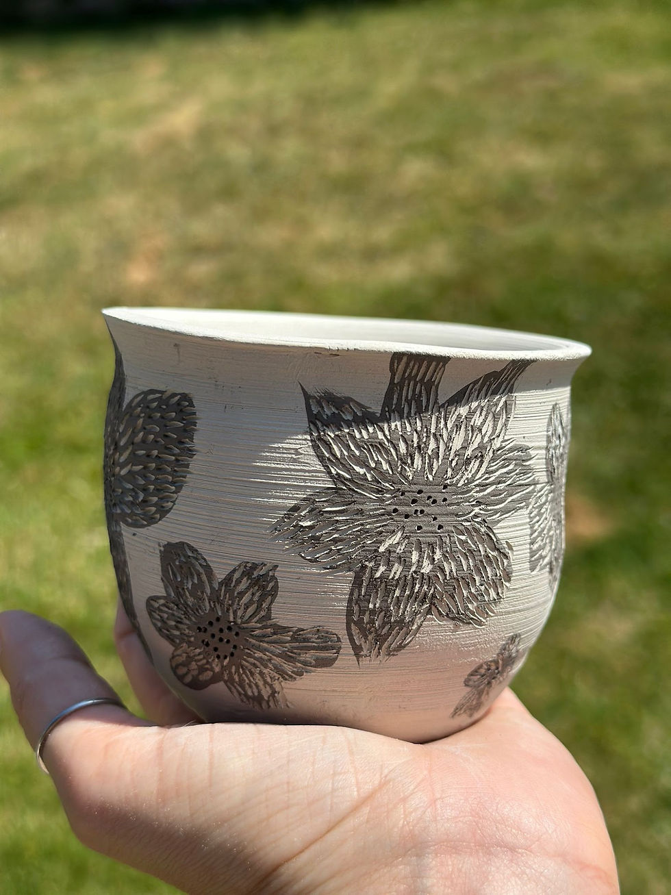 Hand holding a white ceramic pot decorated with carved floral sgraffito patterns outdoors