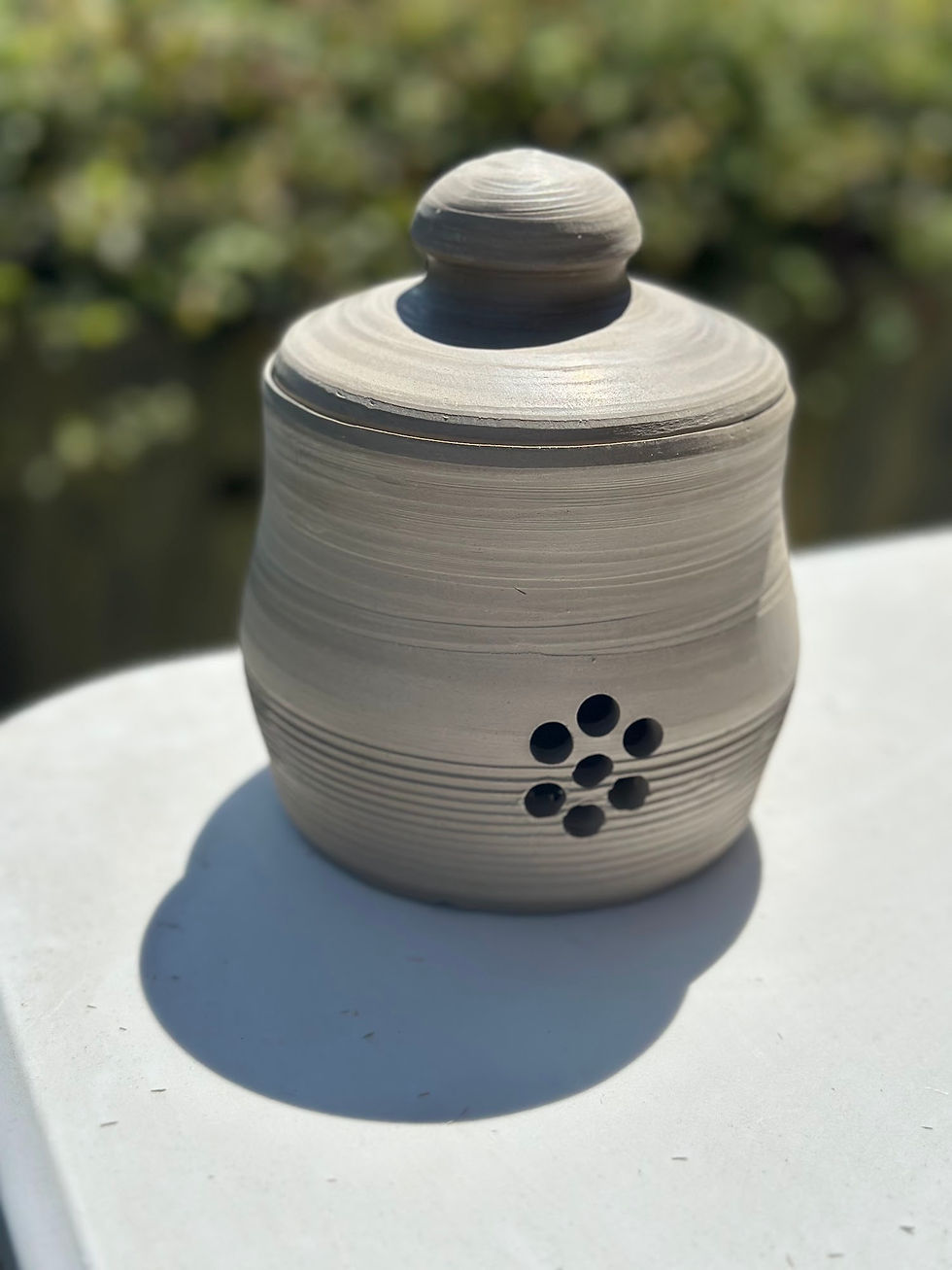 Handcrafted grey ceramic jar with fitted lid and circular ventilation hole pattern on white table