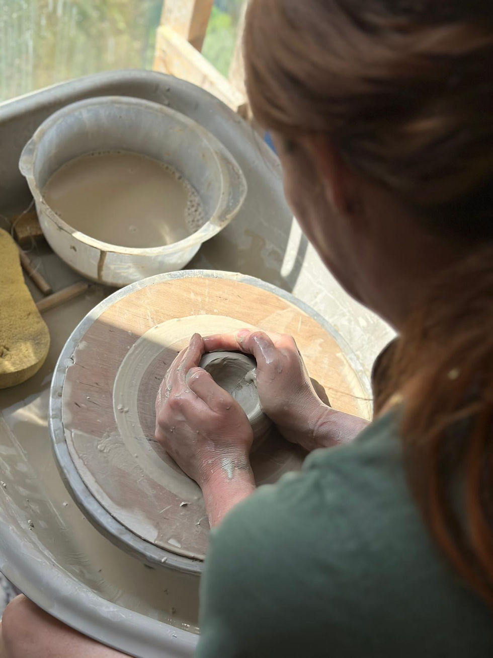Over-the-shoulder view of a potter shaping wet clay on a spinning wheel during a studio class