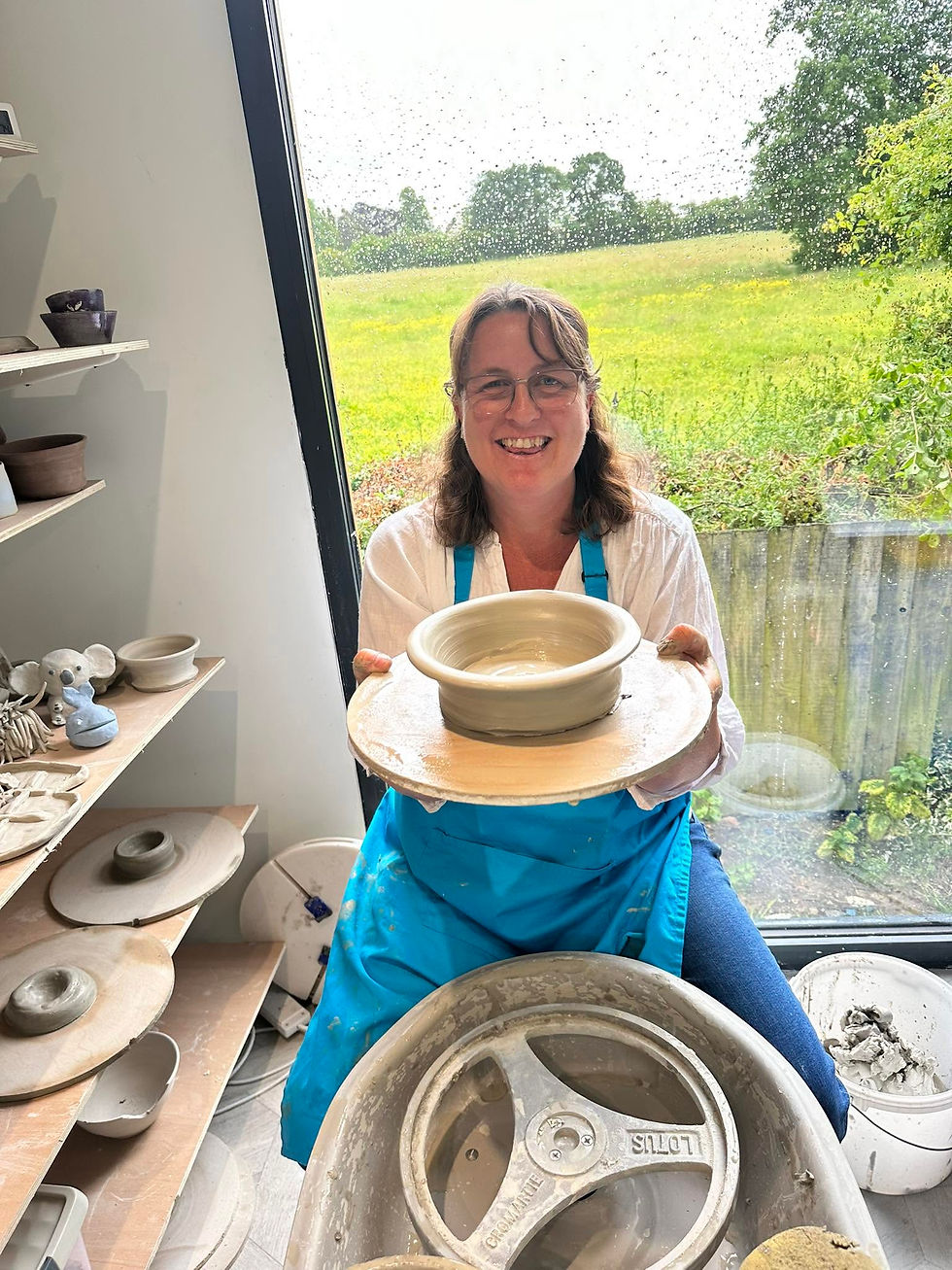 Smiling woman holding a newly thrown ceramic bowl on a bat in a pottery studio