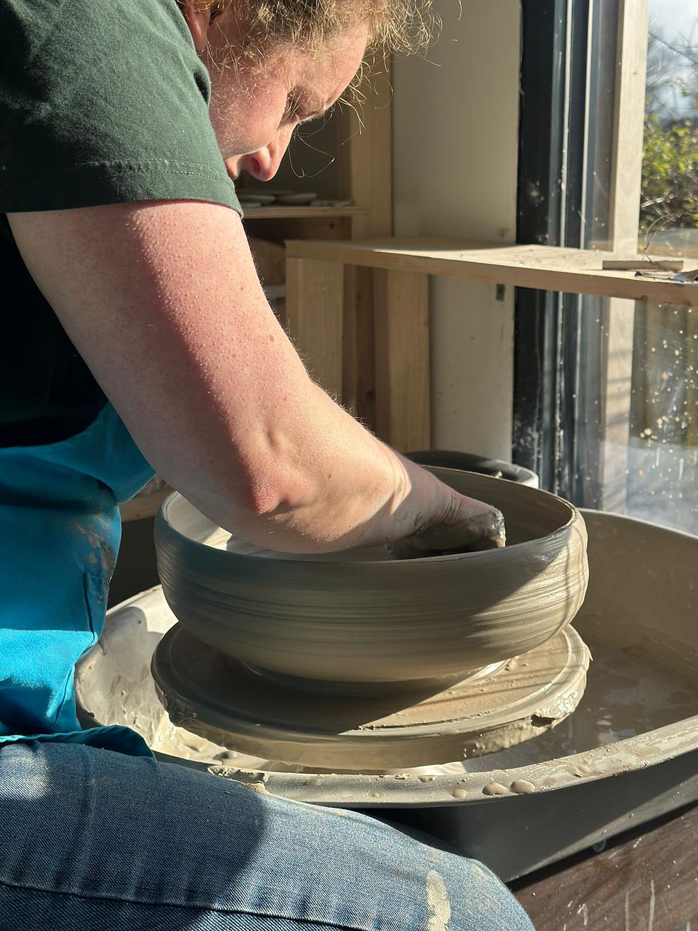 Potter shaping a large clay bowl on a spinning potter's wheel in a bright studio