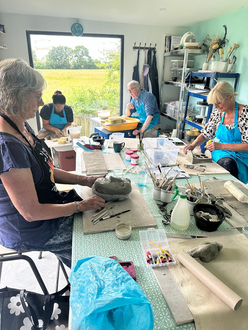Adults crafting clay sculptures and hand-building pottery around a workshop table in a bright ceramic studio