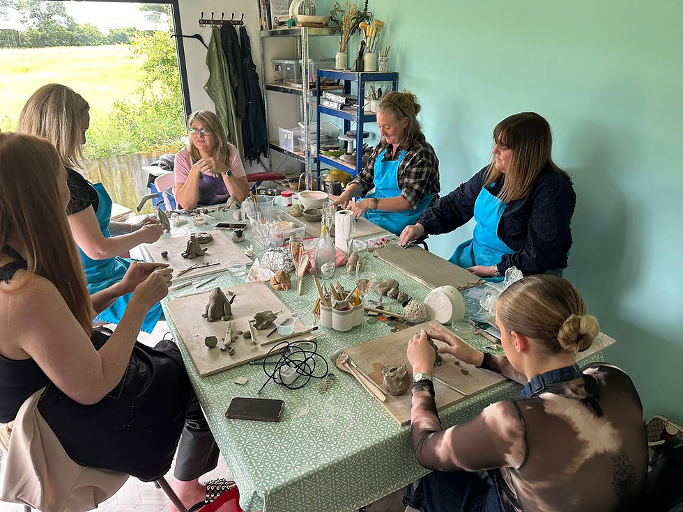 Group of women seated around a craft table working with clay during a pottery class