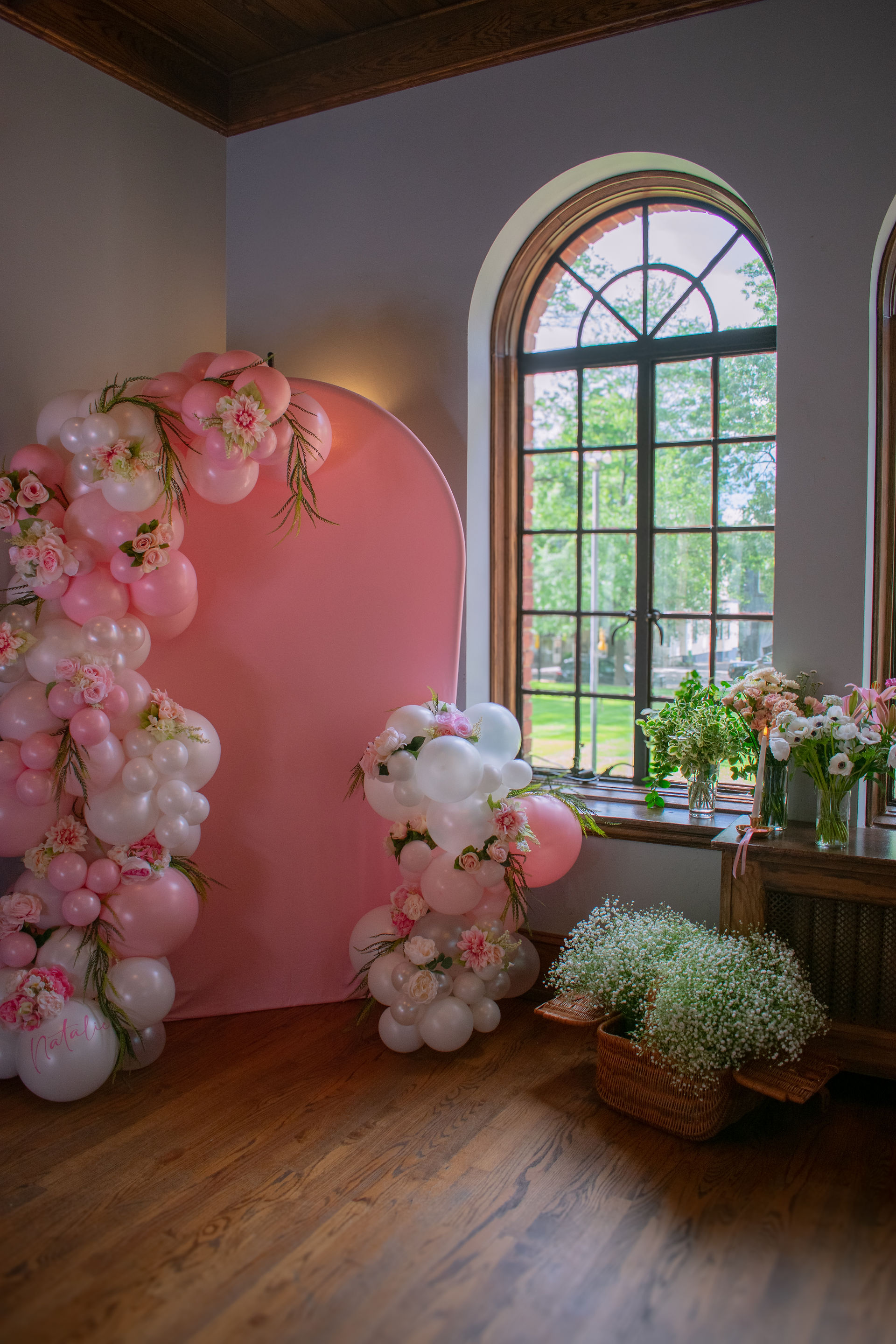 pink backdrop with pink and white balloon arch and flower bar