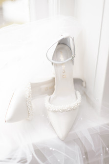 White wedding shoes with beaded top and ankle clips on top of veil in window at Bellevue Hall, in Wilmington, Delaware