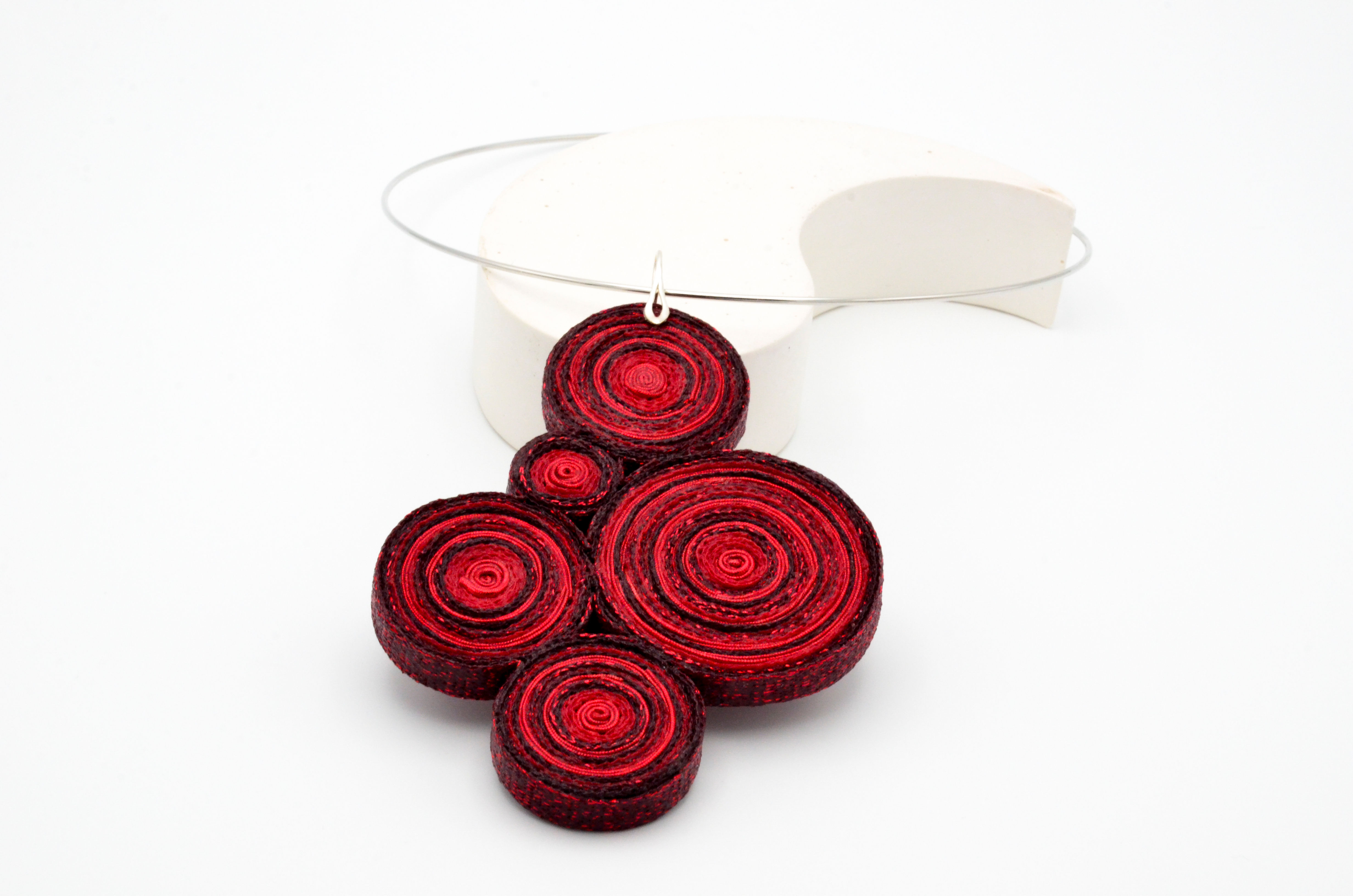 Colgante textil conformado con cinco círculos en diferentes tonalidades de color rojo y gargantilla con baño de plata.