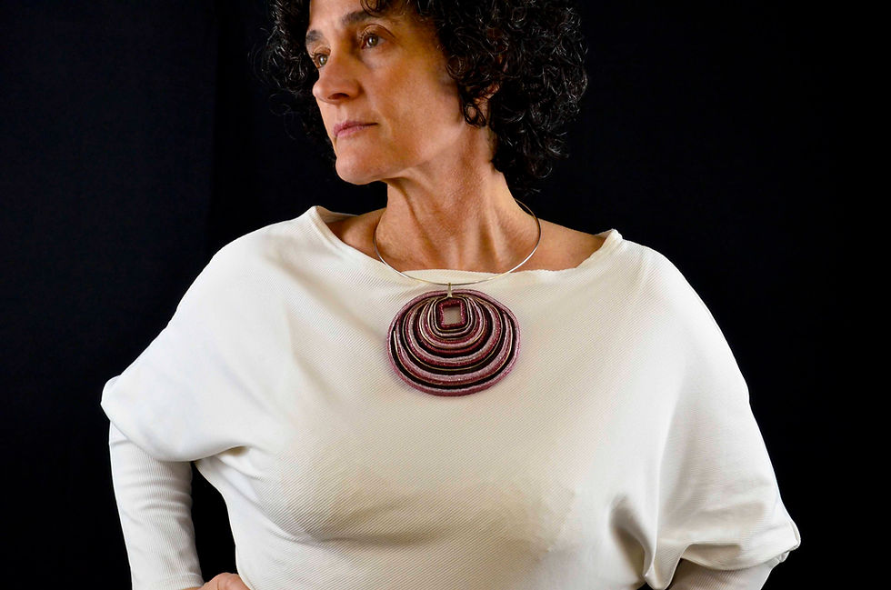Miniatura: Mujer con colgante hecho con cintas de algodón, en colores ciruela y rosa.