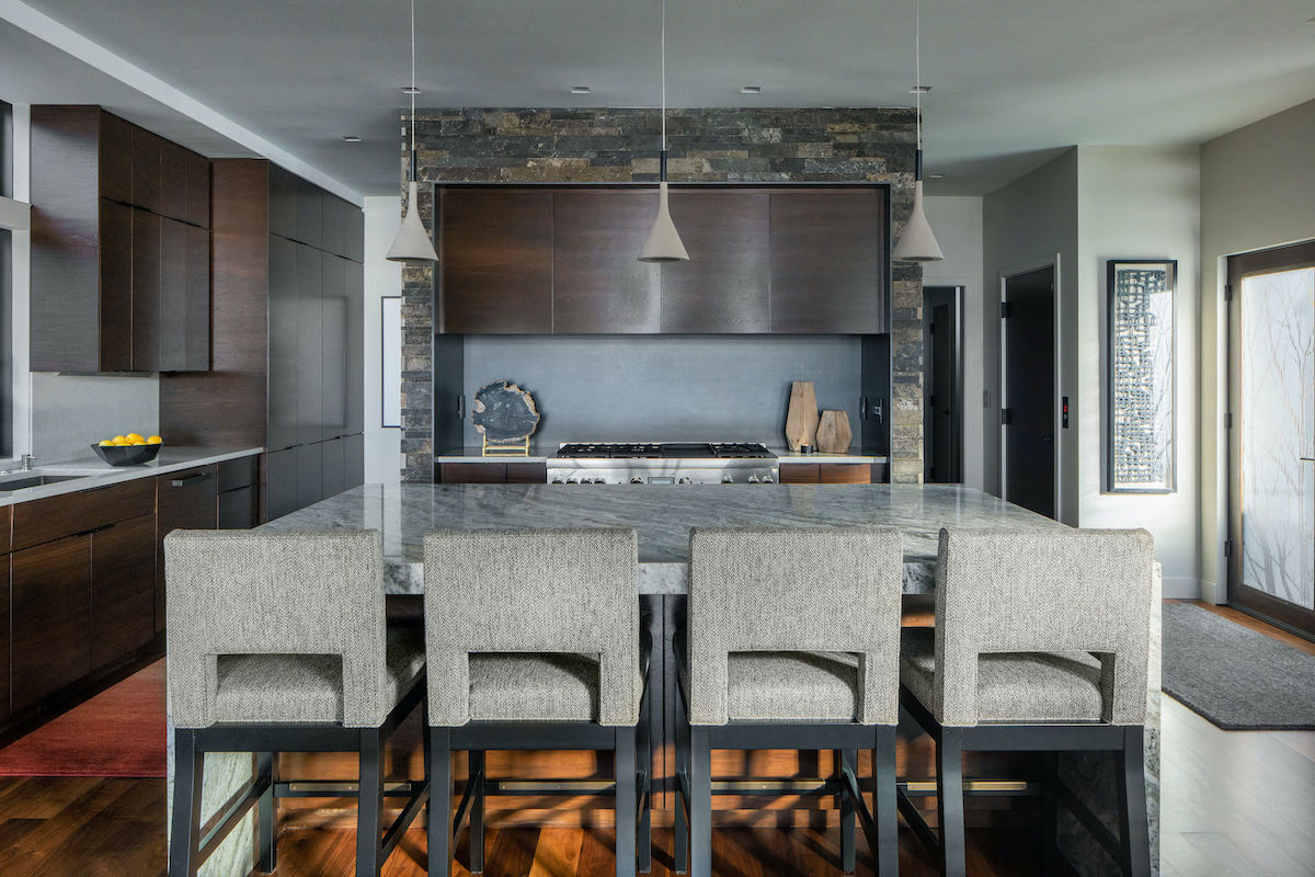 Modern kitchen with gray chairs at a marble island, dark wood cabinets, and a stone accent wall. Bright, minimalistic, and sleek design.