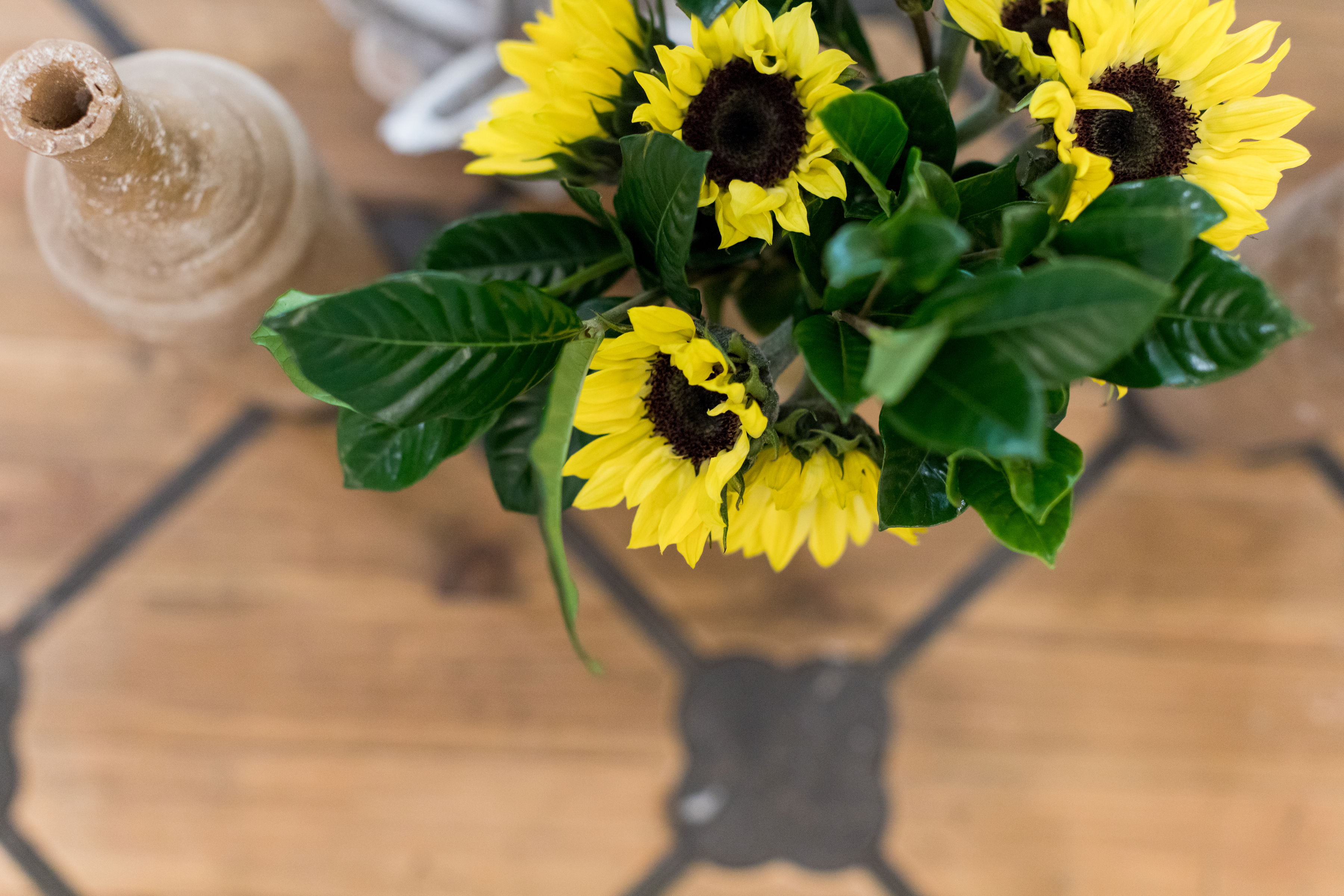 Sunflowers with bright yellow petals in a vase, placed on a wooden table with a patterned design, creating a vibrant and cheerful mood.