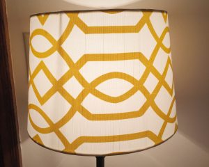 Lamp with yellow geometric pattern on white shade, set against a neutral background. Simple and modern design.