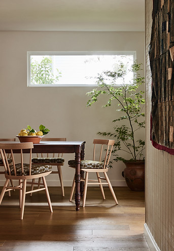 Casual dining room featuring walnut table with turned legs, modern windsor chairs, paneled walls and vintage Japanese wall tapestry.  Seat cushions feature Pierre Frey plaid fabric. 