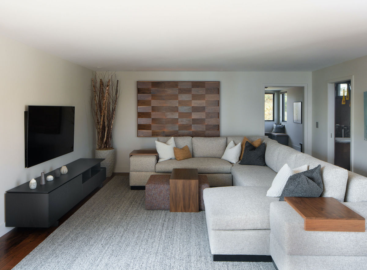 Modern living room with a gray sectional sofa, wooden coffee table, TV, and checkerboard wall art. Neutral tones create a cozy vibe.