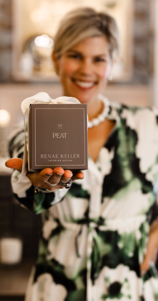 Renae in a floral dress holding a signature candle in a plum box tied with a cream ribbon.