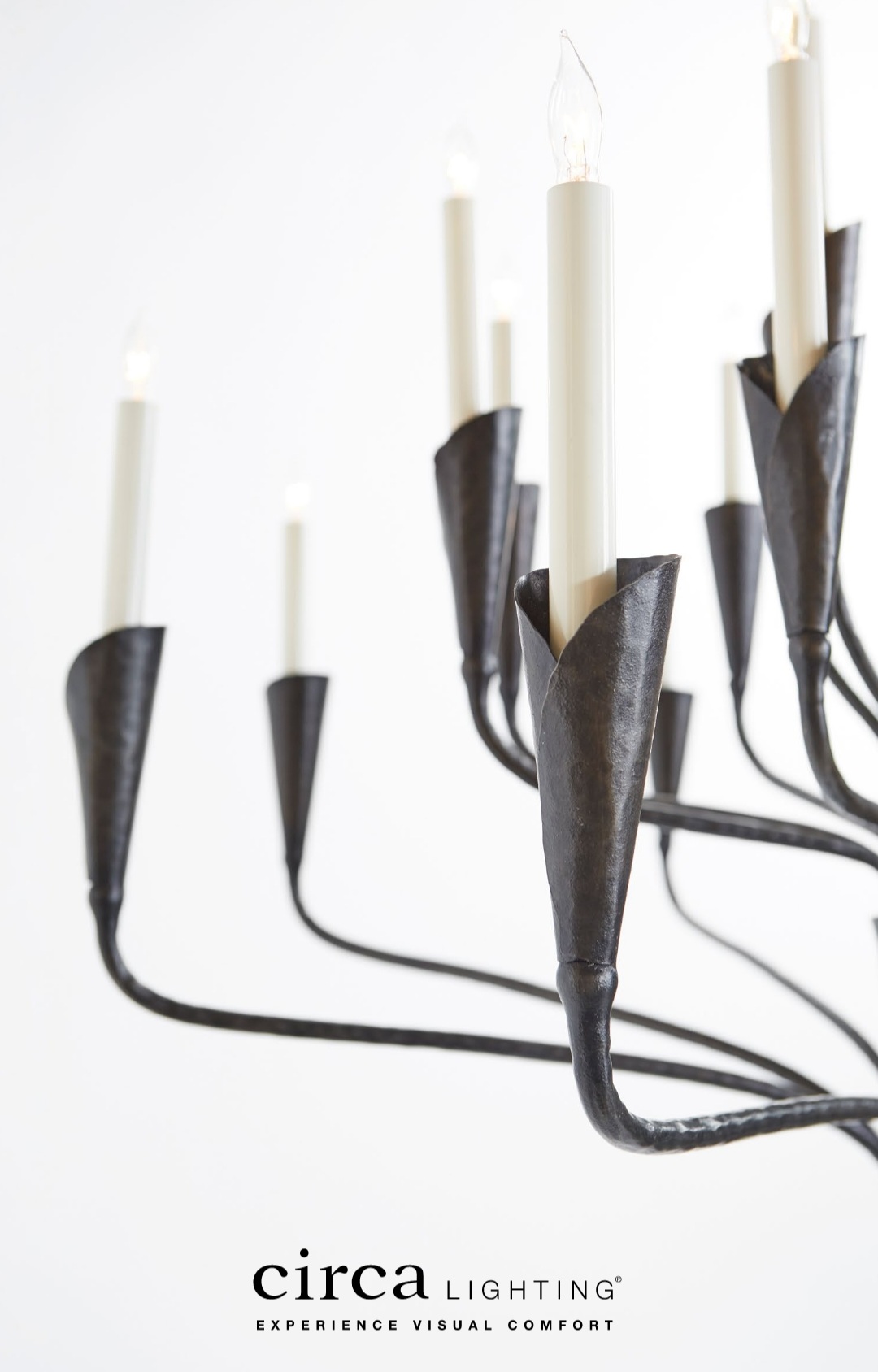 Black iron chandelier with tall white candles against a white background. Text at bottom: circa lighting, experience visual comfort.
