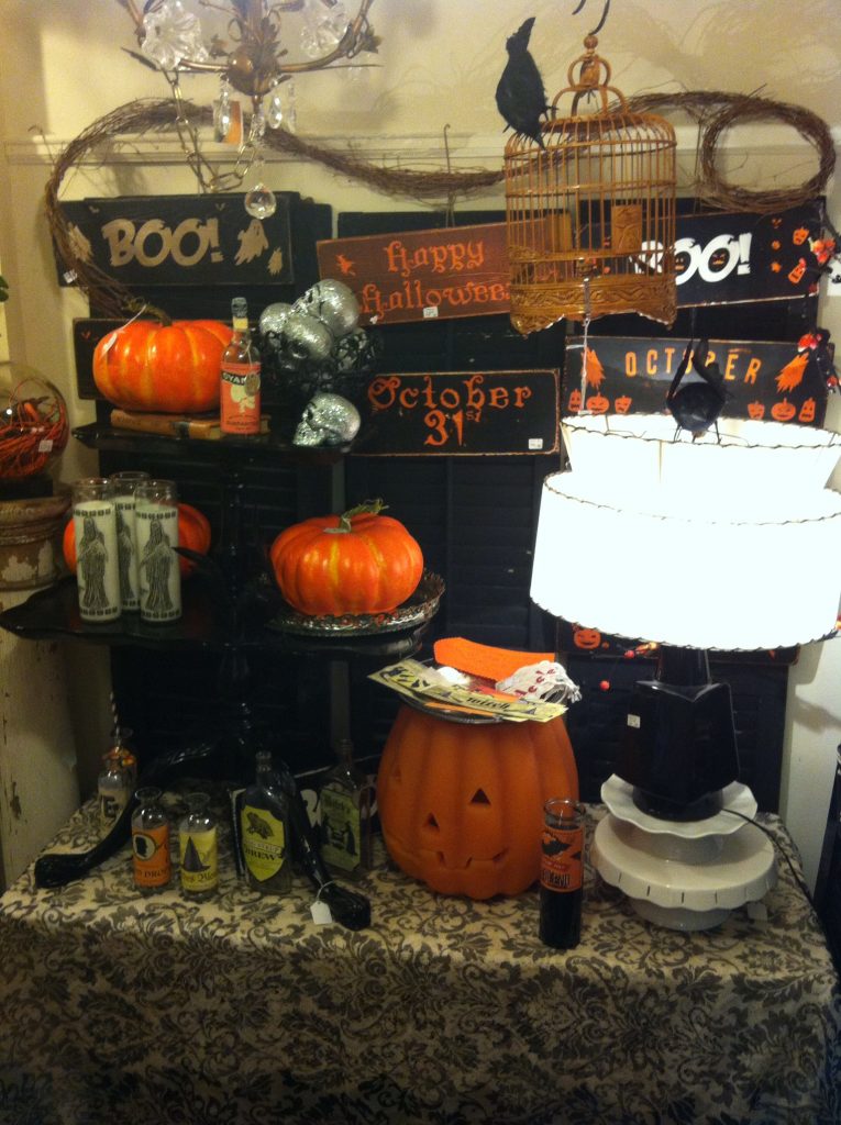 Halloween-themed display with pumpkins, decorative signs reading "Boo!" and "October 31," and a pumpkin-shaped lantern on a patterned tablecloth.