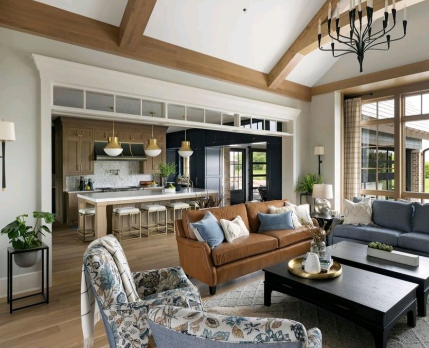 Spacious living room with brown leather sofa, blue armchairs, and dark coffee table. Open kitchen with bar stools. Warm, cozy ambiance.