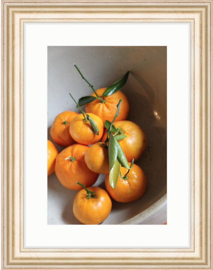 Ripe oranges with green leaves in a white bowl, set against a simple background, framed elegantly in light wood. Bright and fresh mood.