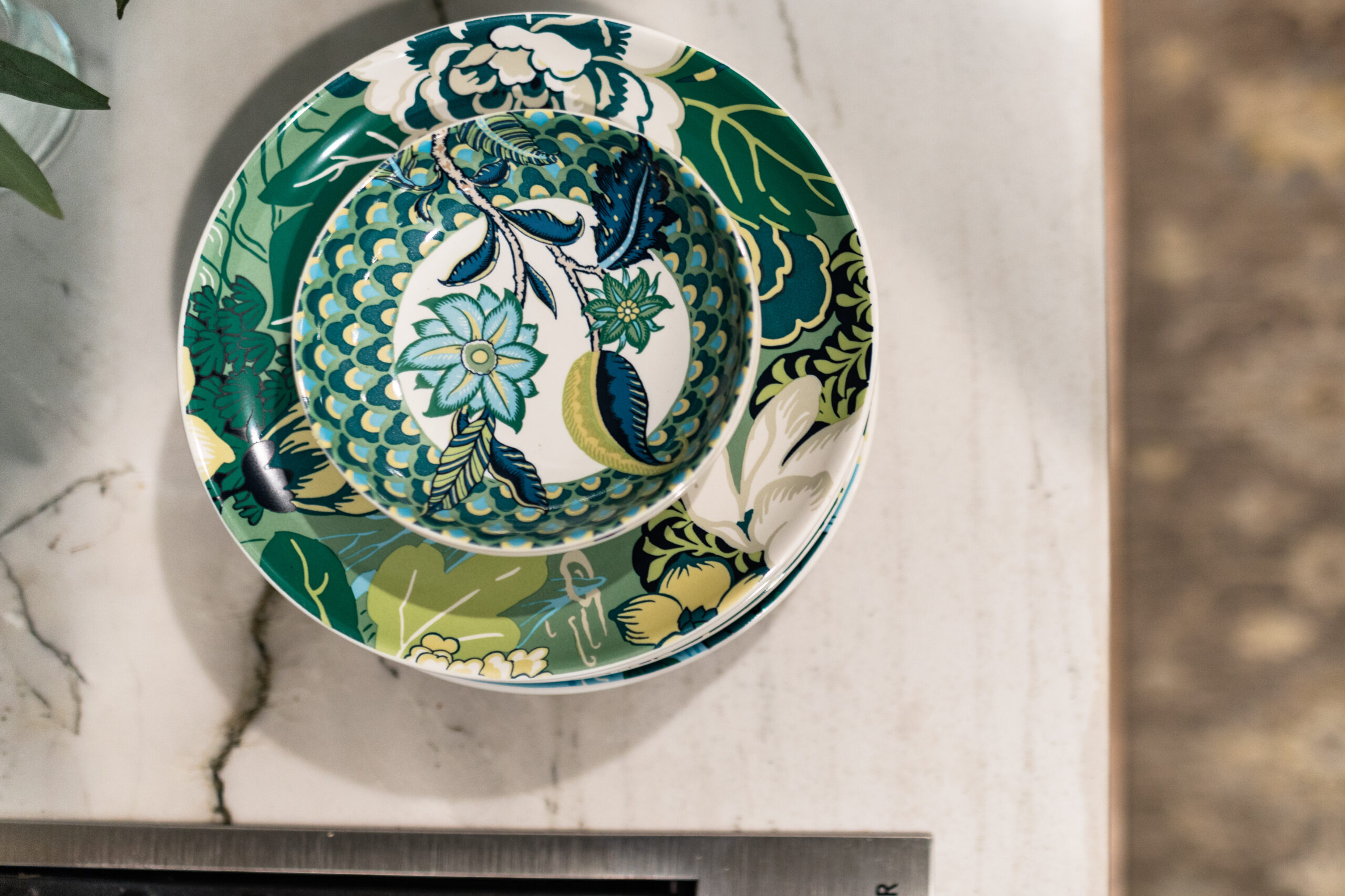Green and blue floral-patterned bowl and plate set on a marble surface. The background includes a blurred brown texture, creating a calm vibe.