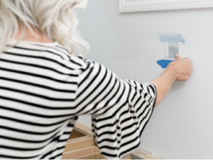 Person in a striped shirt marking a wall with painter's tape; white window frame in background; focused and precise mood.