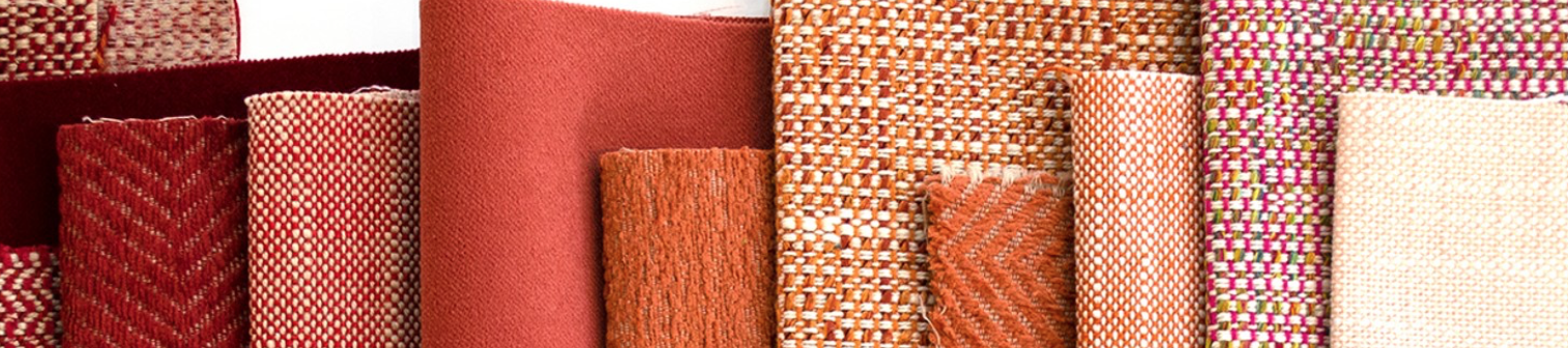 Various textured fabric rolls in red, orange, and beige hues are displayed vertically. Patterns include checkered and woven designs.